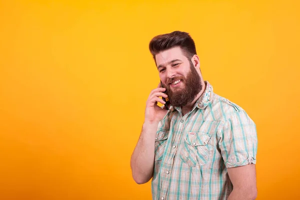 Heureux homme barbu ayant une conversation sur son téléphone sur fond jaune — Photo