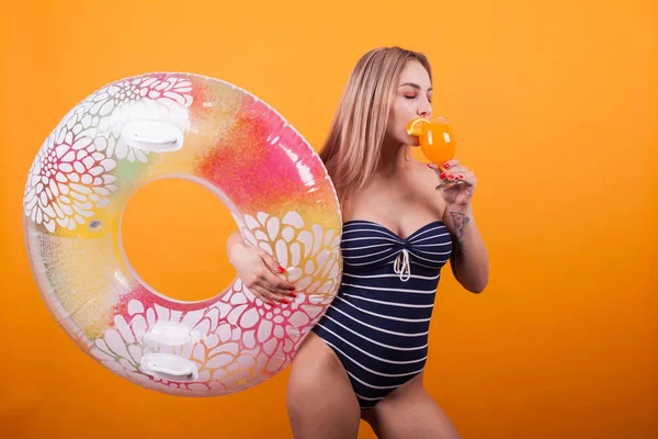 Ganska ung blondin i baddräkt njuter av hennes orange cocktail över gul bakgrund — Stockfoto