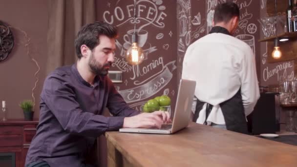 Jovem trabalhando em seu laptop em um balcão de bar — Vídeo de Stock