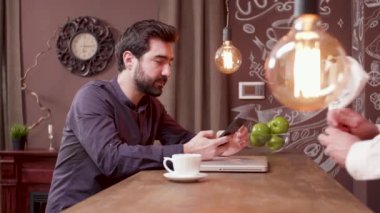 Bardaki genç adam akıllı telefon ekranına bakıyor.