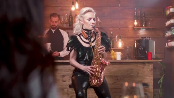 Женщина-зритель поднимает бокал вина, а женщина исполняет песню на саксофоне — стоковое видео
