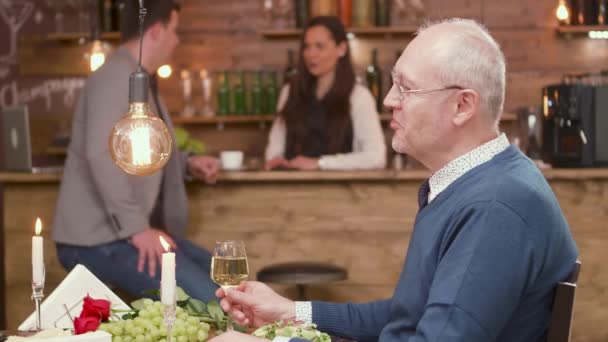 Веселый старик на свидании, звенящий стаканом белого вина — стоковое видео
