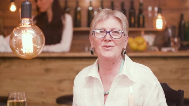 Retrato de una hermosa anciana sentada en una mesa en un bar y hablando con la cámara — Vídeo de stock