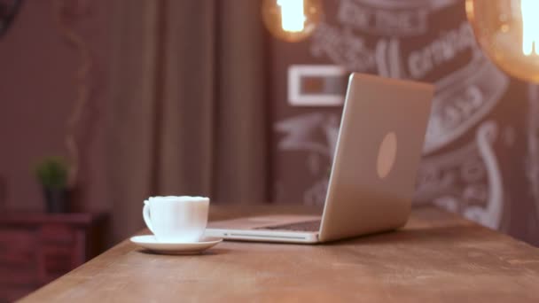En bärbar dator och en vit kopp kaffe på en bar räknare — Stockvideo
