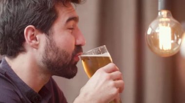 Sakallı genç adam bira içiyor ve barmenle sohbet etmek.