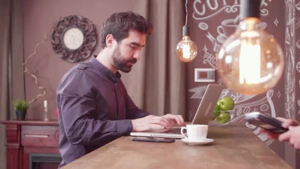 Jonge freelancer die zijn smartphone gebruikt om een betaling te doen aan een balie. — Stockvideo