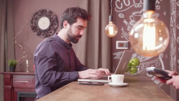 Giovane freelance con il suo smartphone per effettuare un pagamento al bancone di un bar . — Video Stock