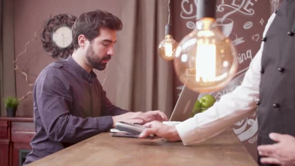 Jeune homme utilisant son smartphone pour effectuer un paiement à un comptoir de bar et part — Video
