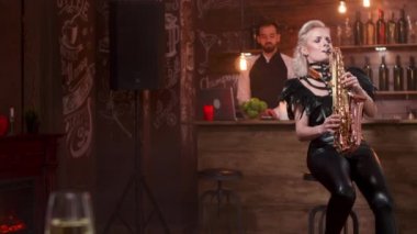 Seksi siyah deri elbiseli kadın saksafonda şarkı söylüyor.