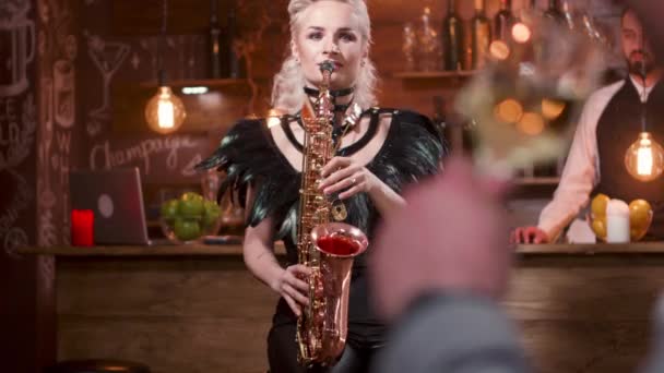 Homme dans le public lève son verre de vin pendant qu'une musicienne joue sur un saxophone — Video