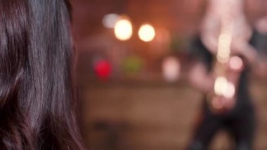 Over the shoulder shot of a woman enjoying a live saxophone performance