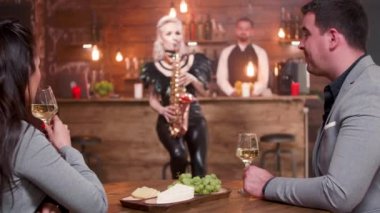 Genç çift bir randevuda şarap içer ve saksafon müziğinin tadını çıkarır.