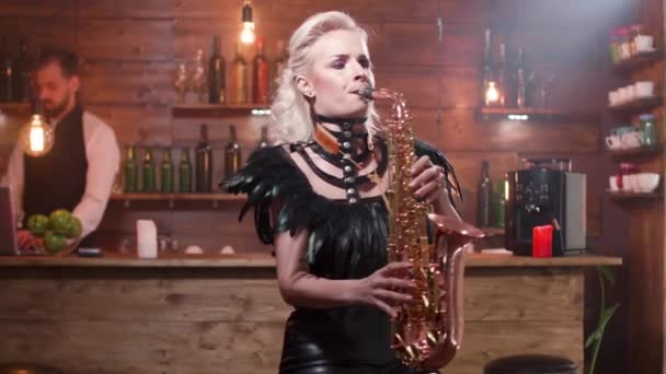 Женщина в сексуальной кожаной одежде на высоком барном стуле играет на саксофоне — стоковое видео