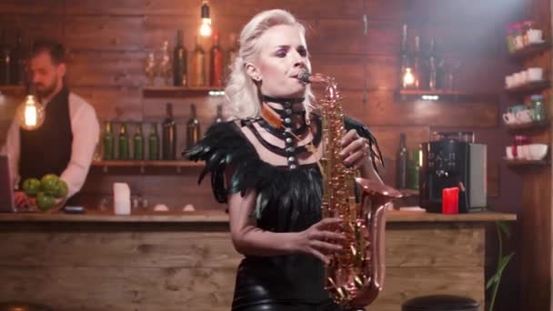 Woman in sexy leather clothes on a high bar chair playing at a saxophone — Stock Video