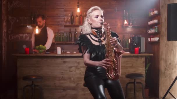 Ładna kobieta w seksownych czarnych skórzanych ubraniach odgrywa piosenkę na saksofonie — Wideo stockowe