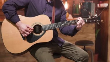 Adam yüksek bir bar sandalyesinde oturur ve akustik gitar çalar