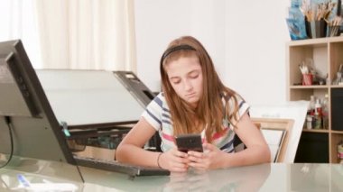 Sıkılmış genç kız bir masada oturur ve onun akıllı telefon üzerinde internette sörf