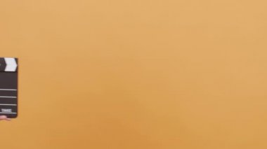 Sarı bir arka plan üzerinde bir clapperboard kullanarak kadın elleri