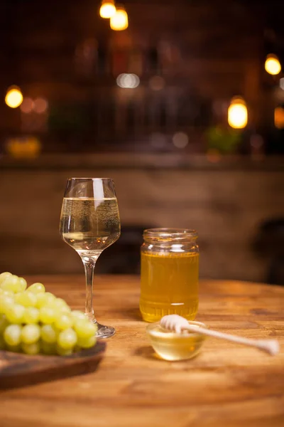 Aranyméz jar mellett egy kifinomult pohár fehér bort egy rusztikus asztal egy Vintage pub — Stock Fotó