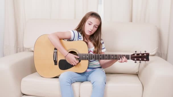 Tiener meisje leren om een zes string akoestische gitaar in de woonkamer te spelen — Stockvideo
