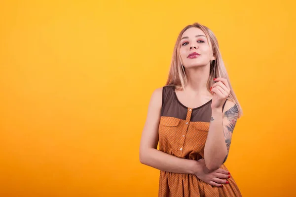 Jolie jeune femme avec tatouage sur sa main en robe décontractée sur fond jaune — Photo