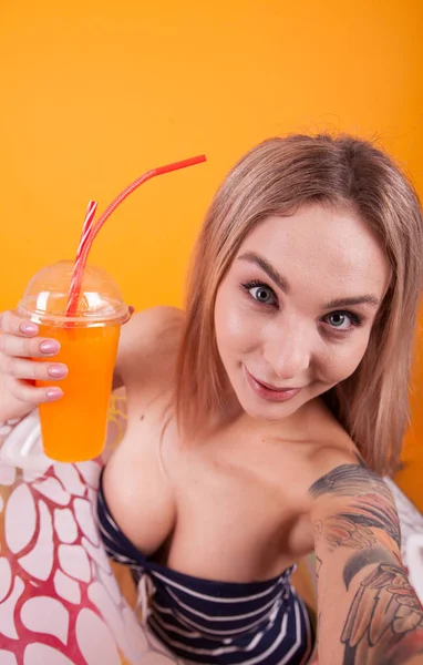 Attraente donna caucasica che si fa un selfie mentre tiene in mano un cocktail di arance fresche e un anello di nuoto — Foto Stock