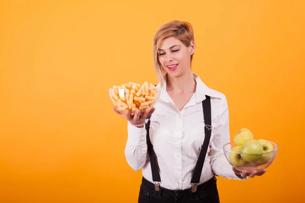 Mujer rubia bonita con pelo corto mirando su tazón de manzanas verdes sobre fondo amarillo . — Foto de Stock