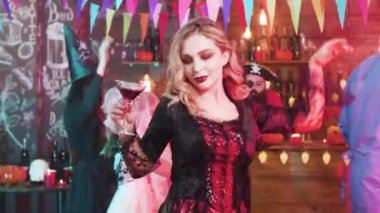 Cadılar Bayramı partisinde elinde bir bardak kanla dans eden genç ve güzel bir kadın.