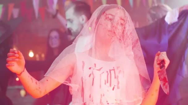 Chica joven con un vestido de novia manchado de sangre con un velo en la cara y un cuchillo ensangrentado como disfraz de Halloween — Vídeos de Stock