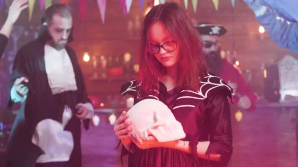 Young girl in eyeglasses disguised as a witch and holds a skull in her hands — 비디오