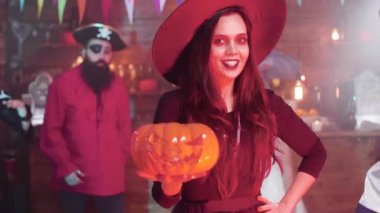 Cadı kostümlü genç kadın elinde oyulmuş bir balkabağı ile şeytanı güldürüyor.