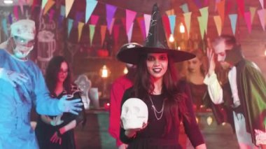 Cadı kostümü giymiş genç bir kadın cadılar bayramı partisinde kafatası tutuyor.