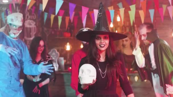 Young woman disguised in witch costume hold a skull in her hands at a halloween party — Stock Video