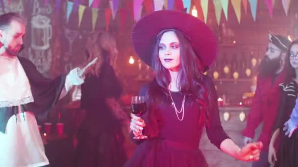 Attractive woman disguised as a witch dances with a glass of blood at a halloween party — Stock Video