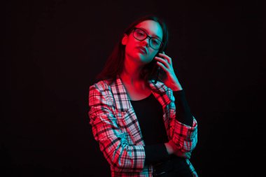 Güzel genç kız telefonda konuşurken ve renkli Aydınlatma ile stüdyoda kameraya bakıyor