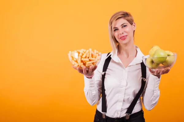 Mujer linda con camisa blanca sosteniendo un tazón de bollos de maíz y manzanas verdes sobre fondo amarillo . — Foto de Stock