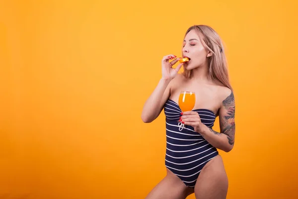 Atrakcyjna kobieta w stroju kąpielowym i smaczne lato koktajl gryzący pomarańczowy plasterek — Zdjęcie stockowe