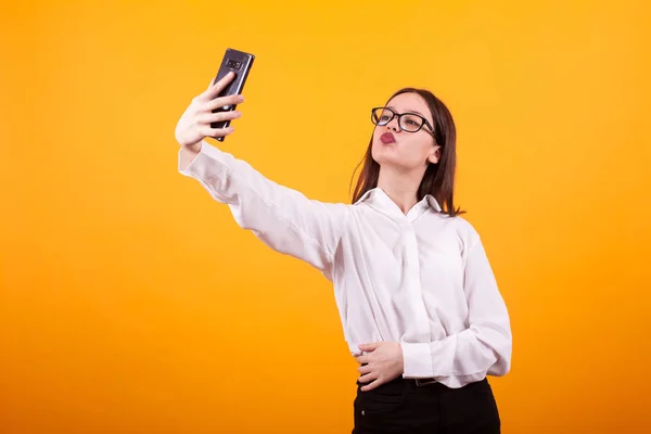 Jolie jeune fille faire un selfie et faire des lèvres de canard à la caméra en studio sur fond jaune — Photo