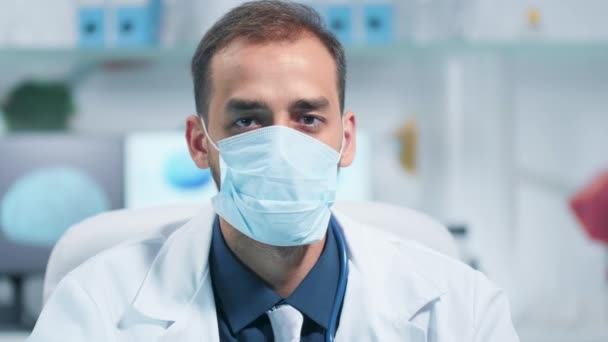 Retrato de un médico con una máscara medicinal y mirando a la cámara — Vídeos de Stock