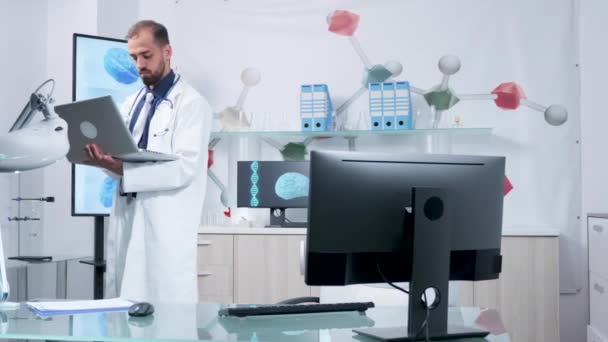 Doktor w jego nowoczesnym biurze stoi i wpisując na swoim laptopie — Wideo stockowe