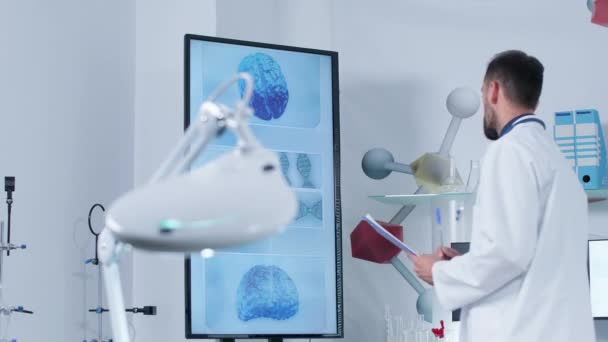 Dolly shot of a scientist in modern research center looking at big TV — Stock Video