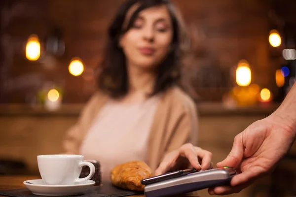 커피 숍에서 무선 지불을 사용하여 휴대 전화로 지불하는 매력적인 여성의 사진 — 스톡 사진