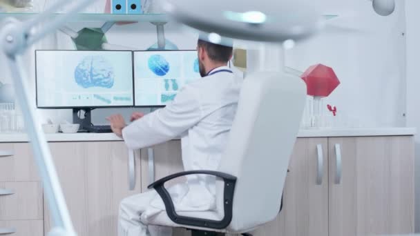 Arzt arbeitet in moderner Forschungseinrichtung mit 3D-Hirnscans auf Monitoren — Stockvideo