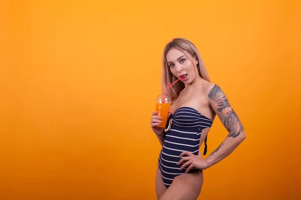 Bela jovem sexy mulher no natação terno beber verão bebida sobre amarelo fundo — Fotografia de Stock