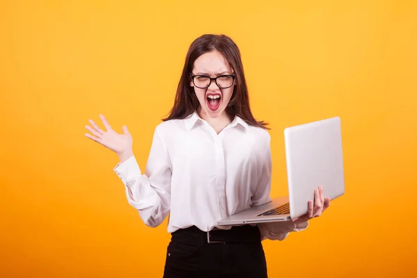 Porträtt av tonårsflickan skrikande och hållande henne laptop från upphetsning i studion över gult bakgrunden — Stockfoto