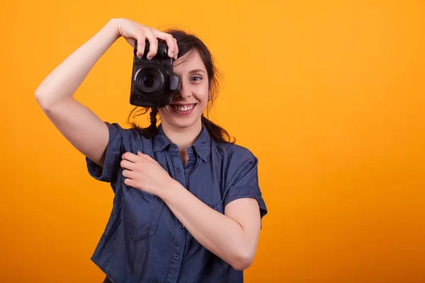 Woman photographer is taking images with dslr camera in studio over yellow background