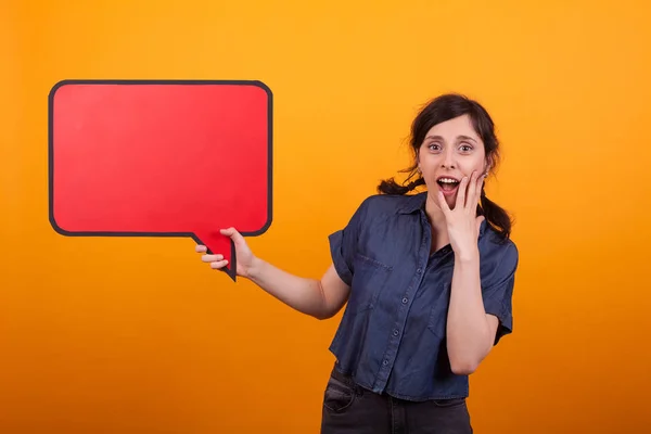 Geschokt jonge vrouw met een toespraak bubble tegen een gele achtergrond in Studio — Stockfoto