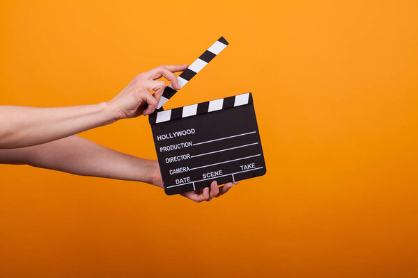 Woman holding professional film slate, movie clapper board in studio over yellow background