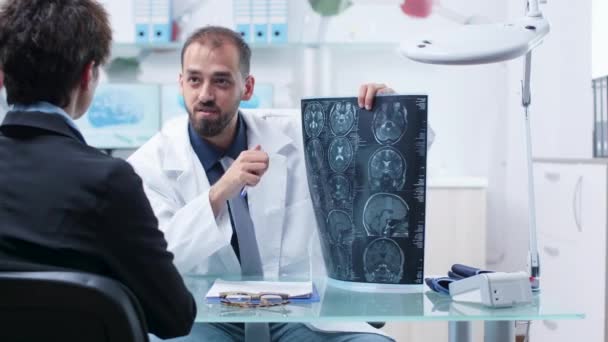 Doctor at desk in modern research facility showing X ray scans to patient — Stock Video