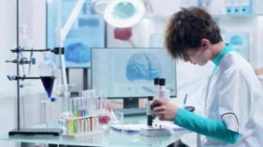 Modern laboratuarda çalışan tıp kıyafetleri içinde genç bir kadın bilim adamı.